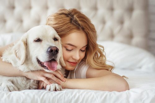 female-owner-hugging-dog-while-laying-on-bed